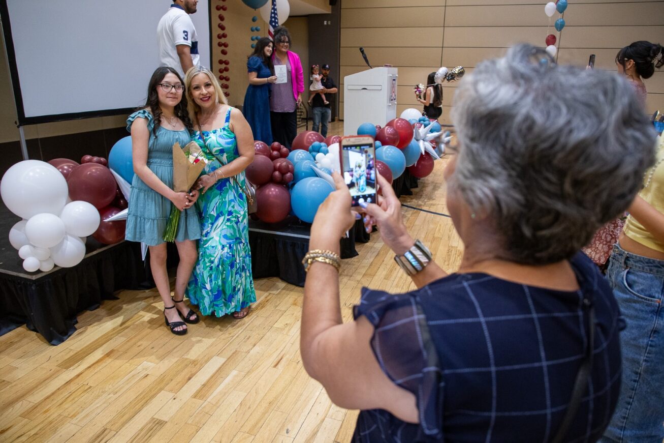 A woman takes a photo of a TUVA 8th grader and her mom after the ceremony