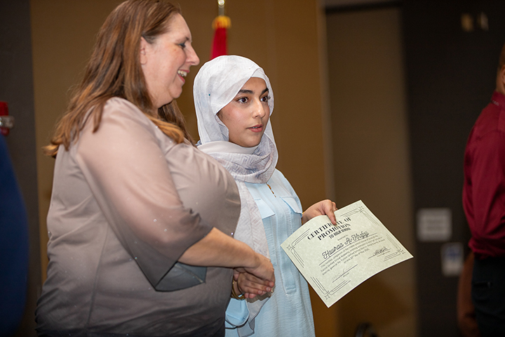 A woman shakes hands with a promoting 8th grader