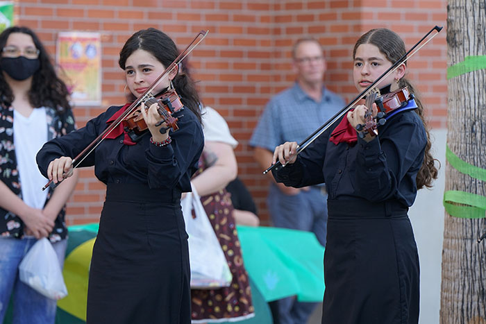 Two girls play violin for people watching outside