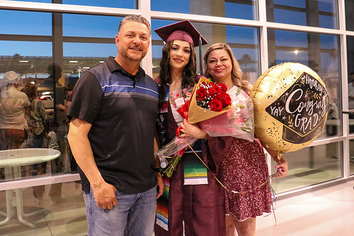 A graduate smiles with her parents while holding flowers