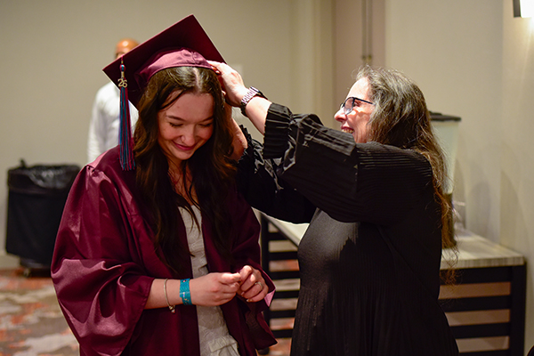 A graduate smiles as she has her cap adjusted